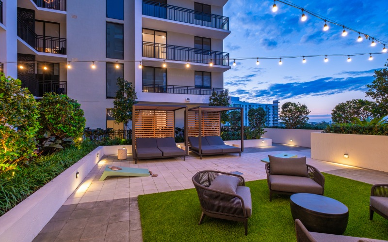 Outdoor rooftop terrace at The Holly at Soleste in Hollywood, FL featuring lounge seating, cabanas, string lights, and landscaped greenery at sunset