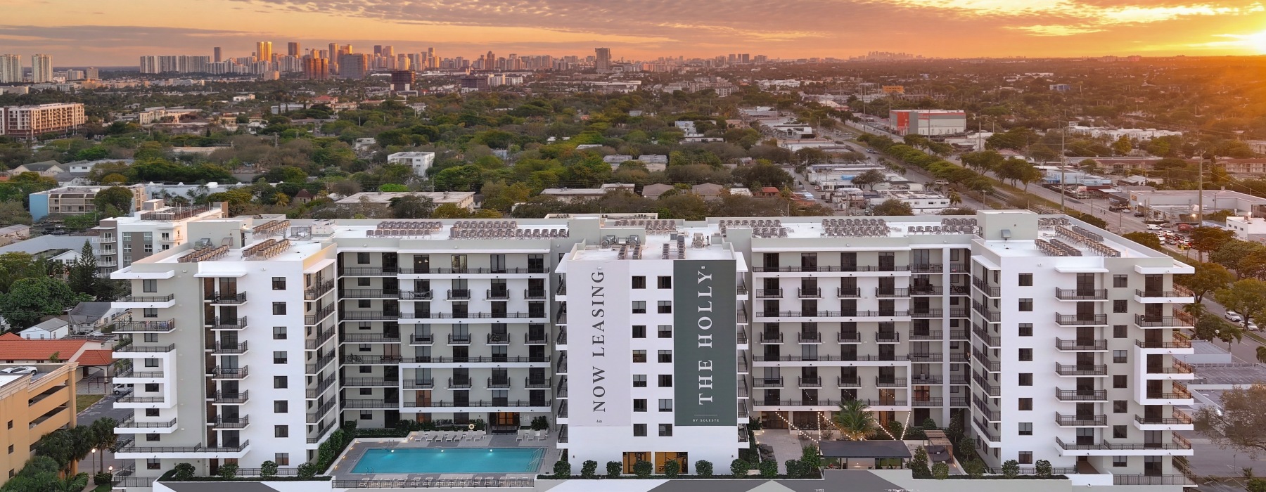 Aerial view of The Holly luxury apartments in downtown Hollywood, FL featuring a rooftop pool deck, modern balconies, and covered parking garage.